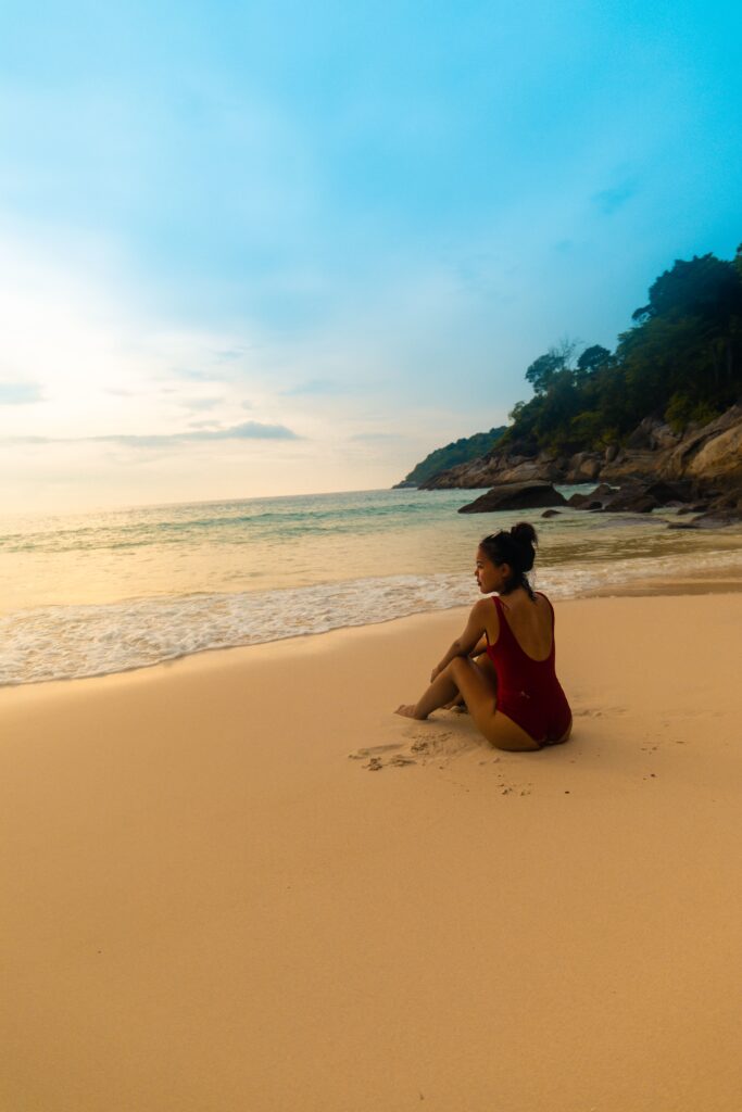 vertical shot of a female wearing a red swimsuit sitting at the sandy beach during sunrise
